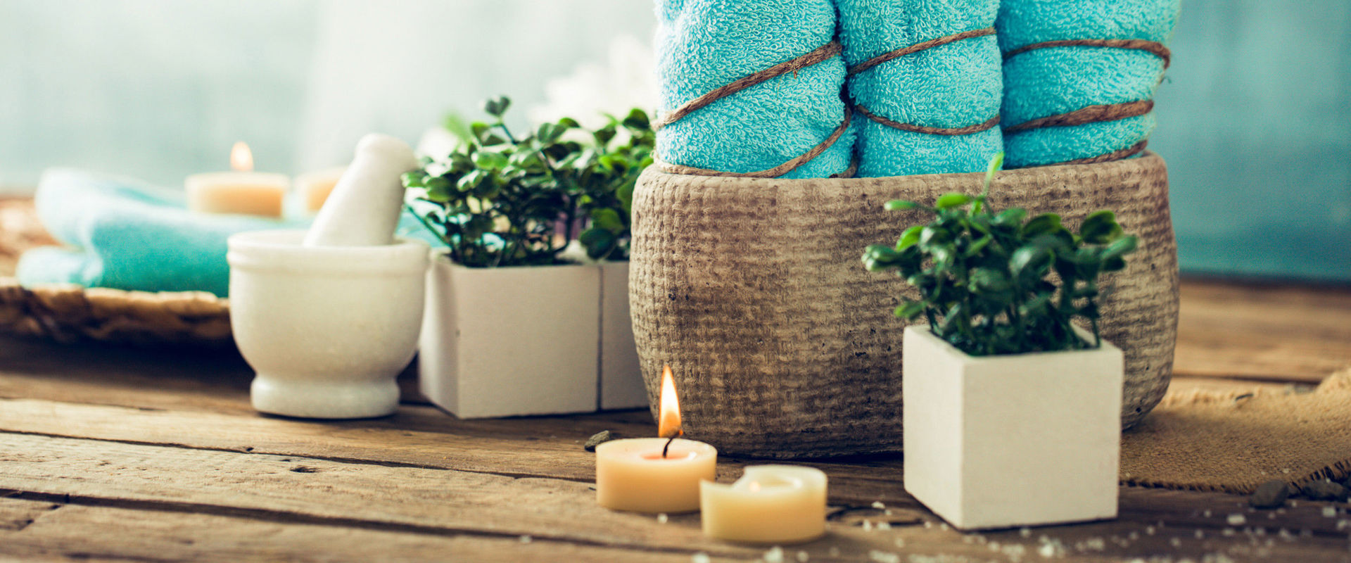 Wellness products 3 turquoise towels, candles and flowers stand on a wooden base.