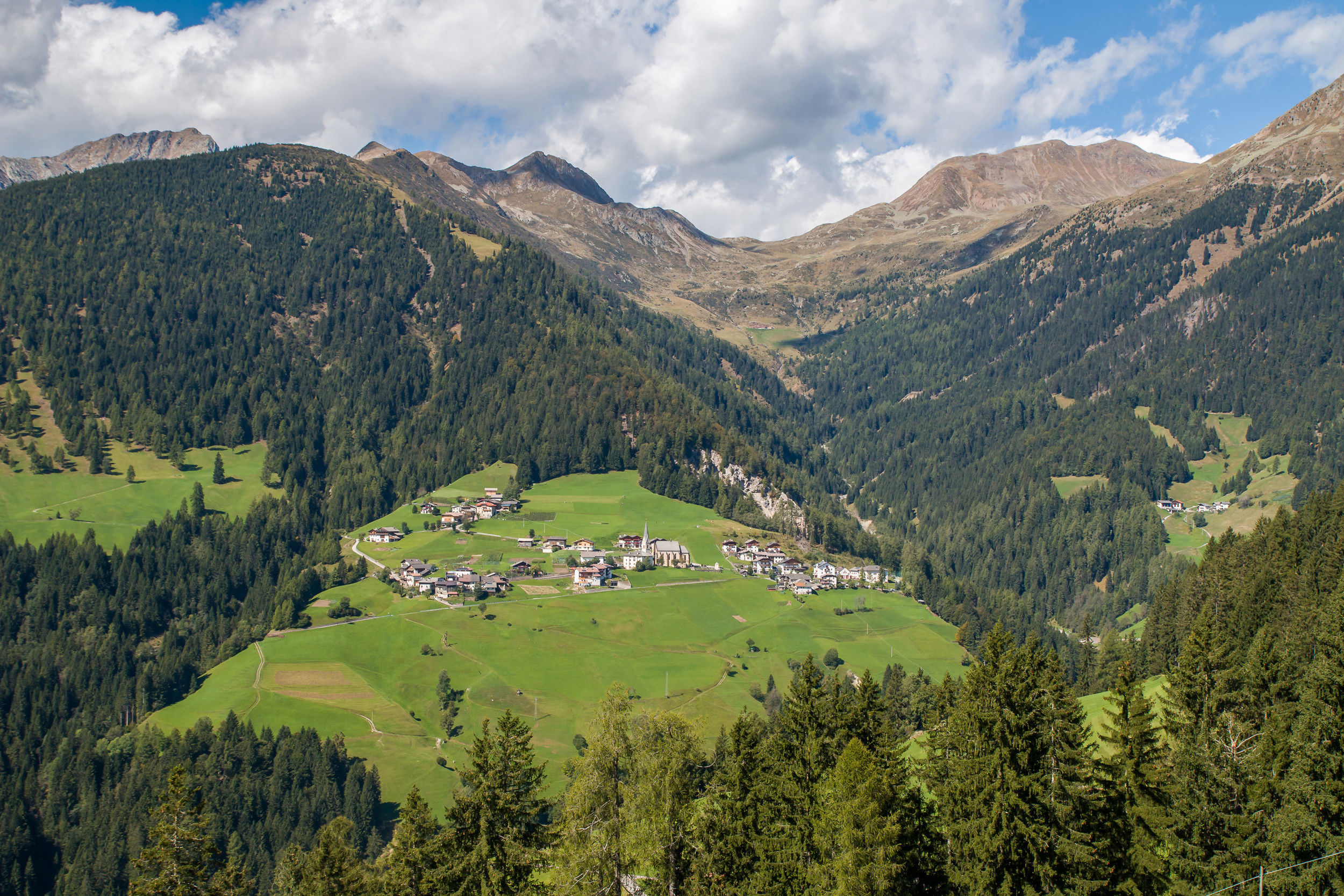 The small mountain village of Proveis amidst lush green meadows and surrounded by dense coniferous forests.