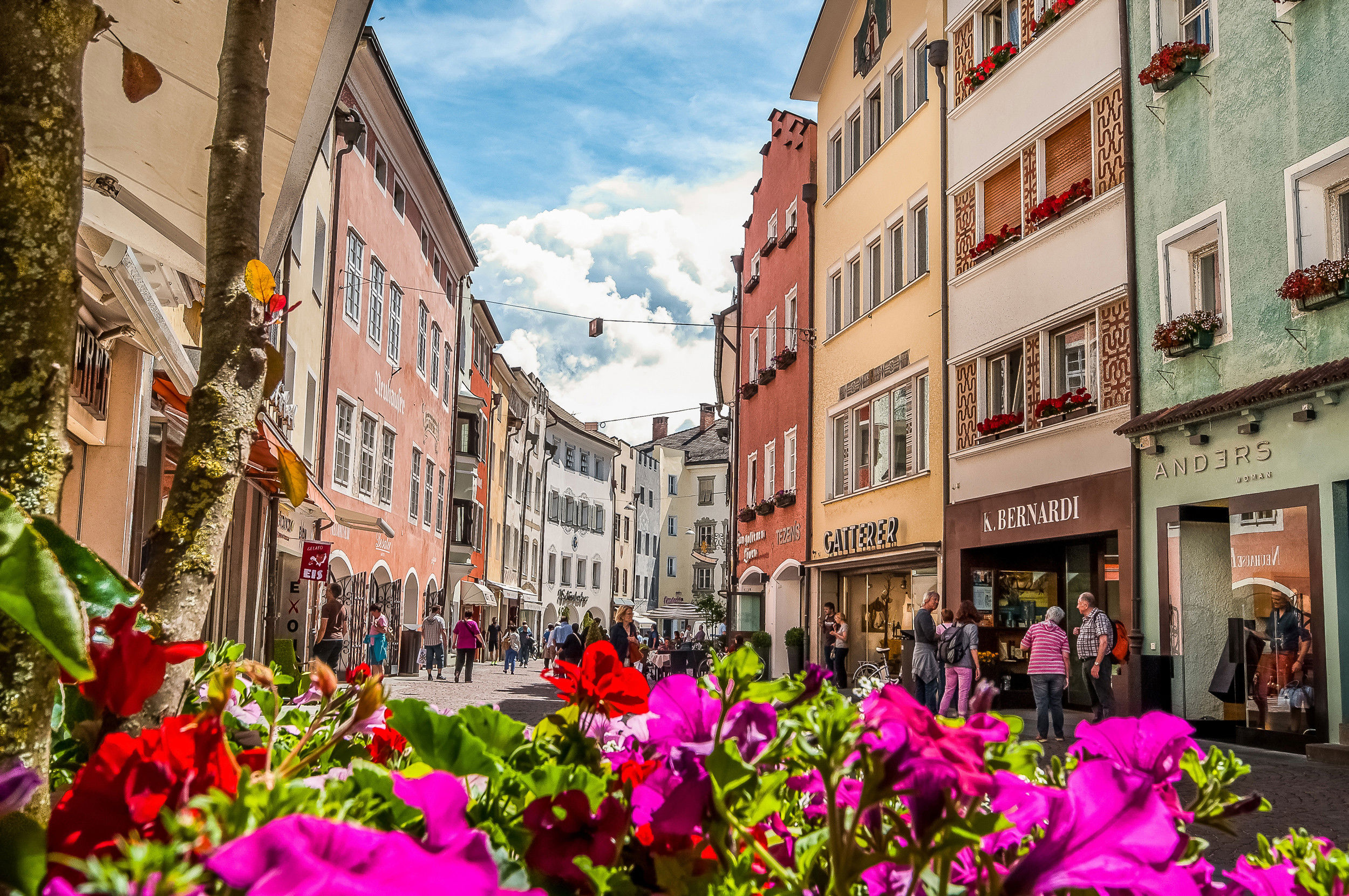 Lively city centre with colourful house facades framed by bright summer flowers.