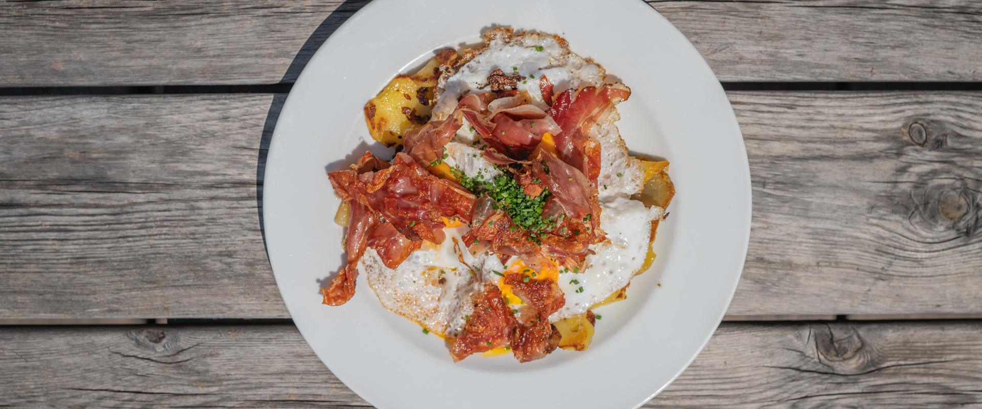 A plate on a wooden table with roast potatoes, bacon and eggs