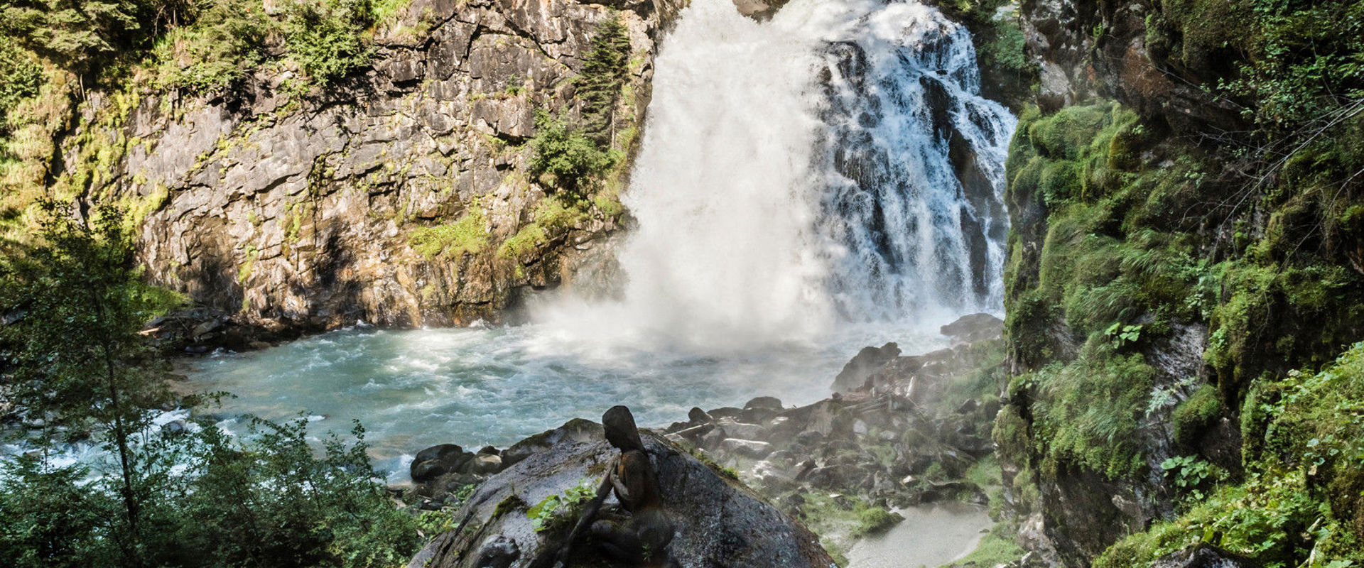 Reinbach waterfalls Waterfall flowing down over the rocks. To the left and right side of the picture you can see steep rock faces with tall conifers.