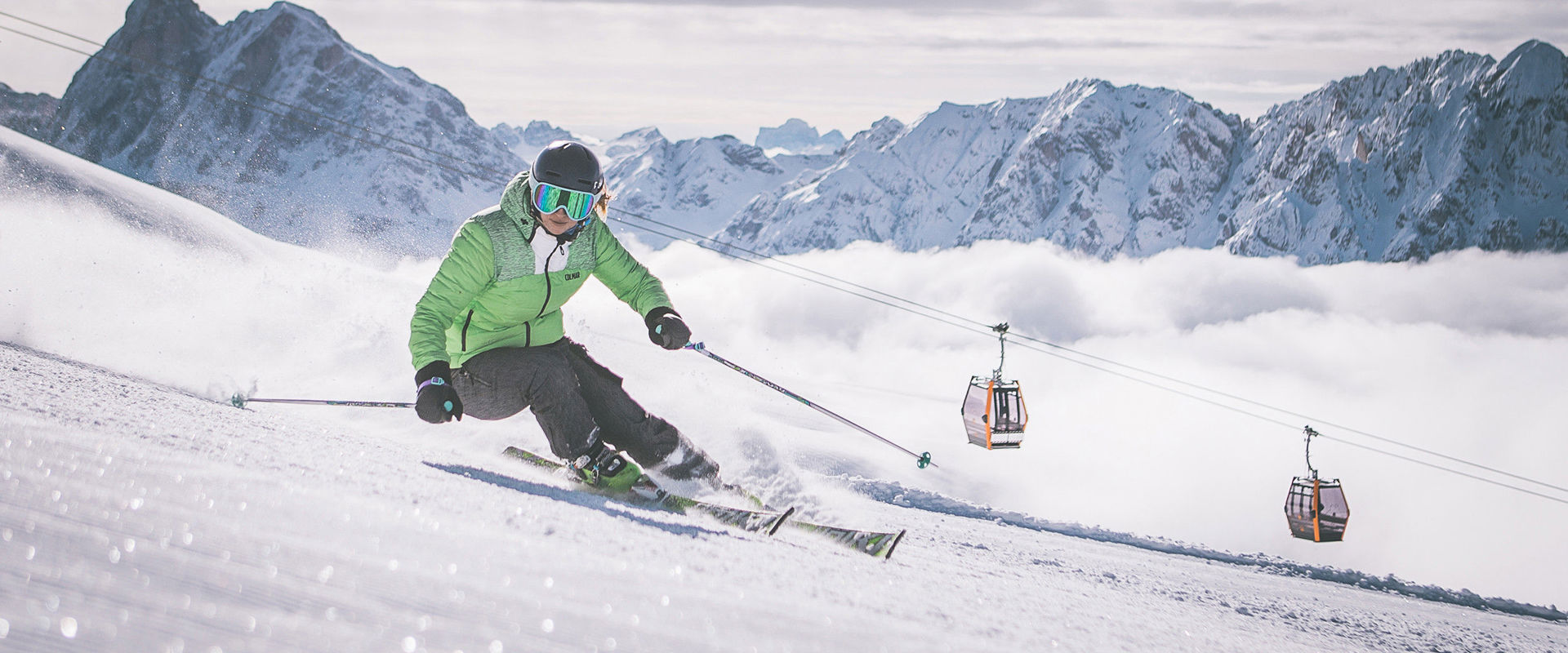 Skier goes down the slope. In the background one can see the gondola and the snow-covered mountain peaks.