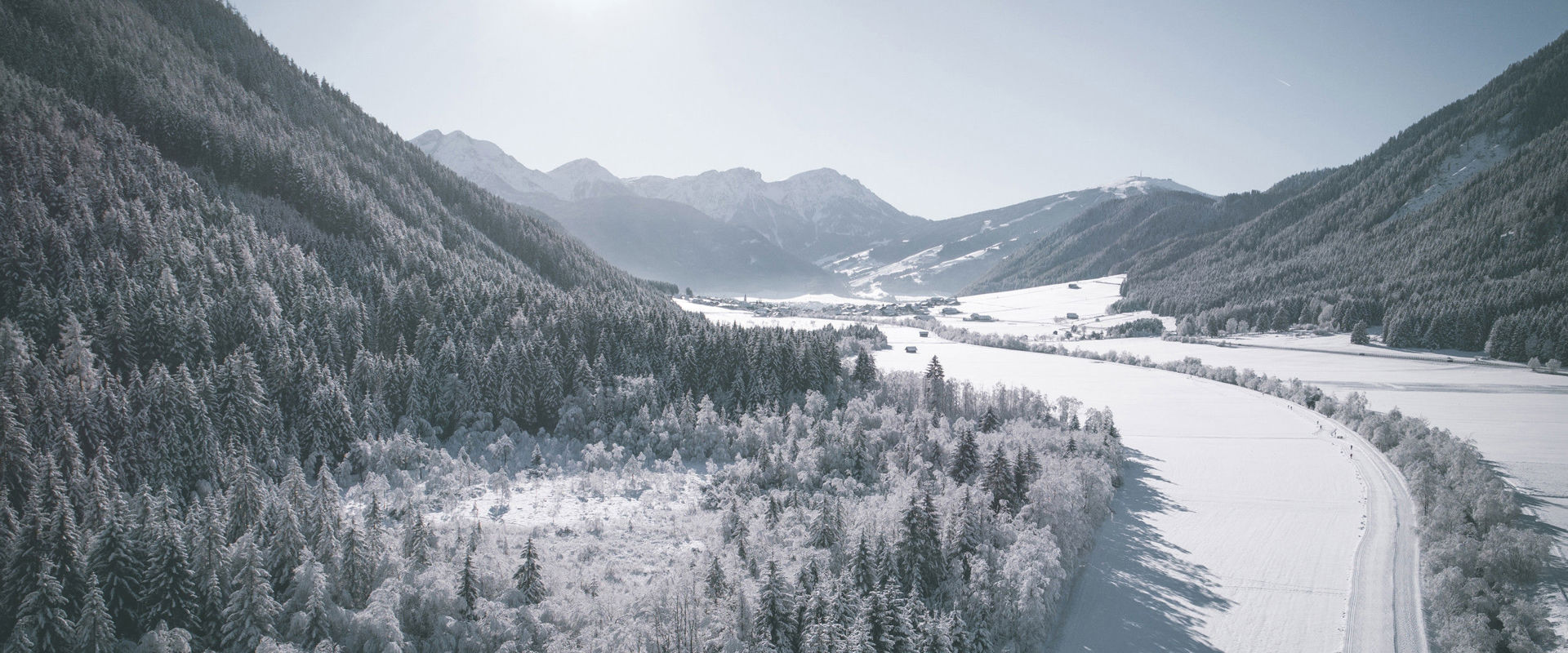 Winter in Antholz. View of snow-covered, sunny valley with cross-country ski trail and village in the background.
