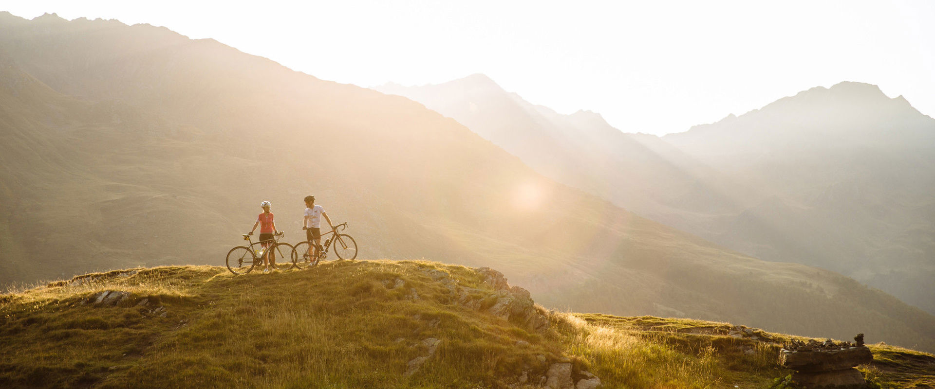 Cycling in the mountains 2 cyclists stand in the middle of a breathtaking mountain landscape.