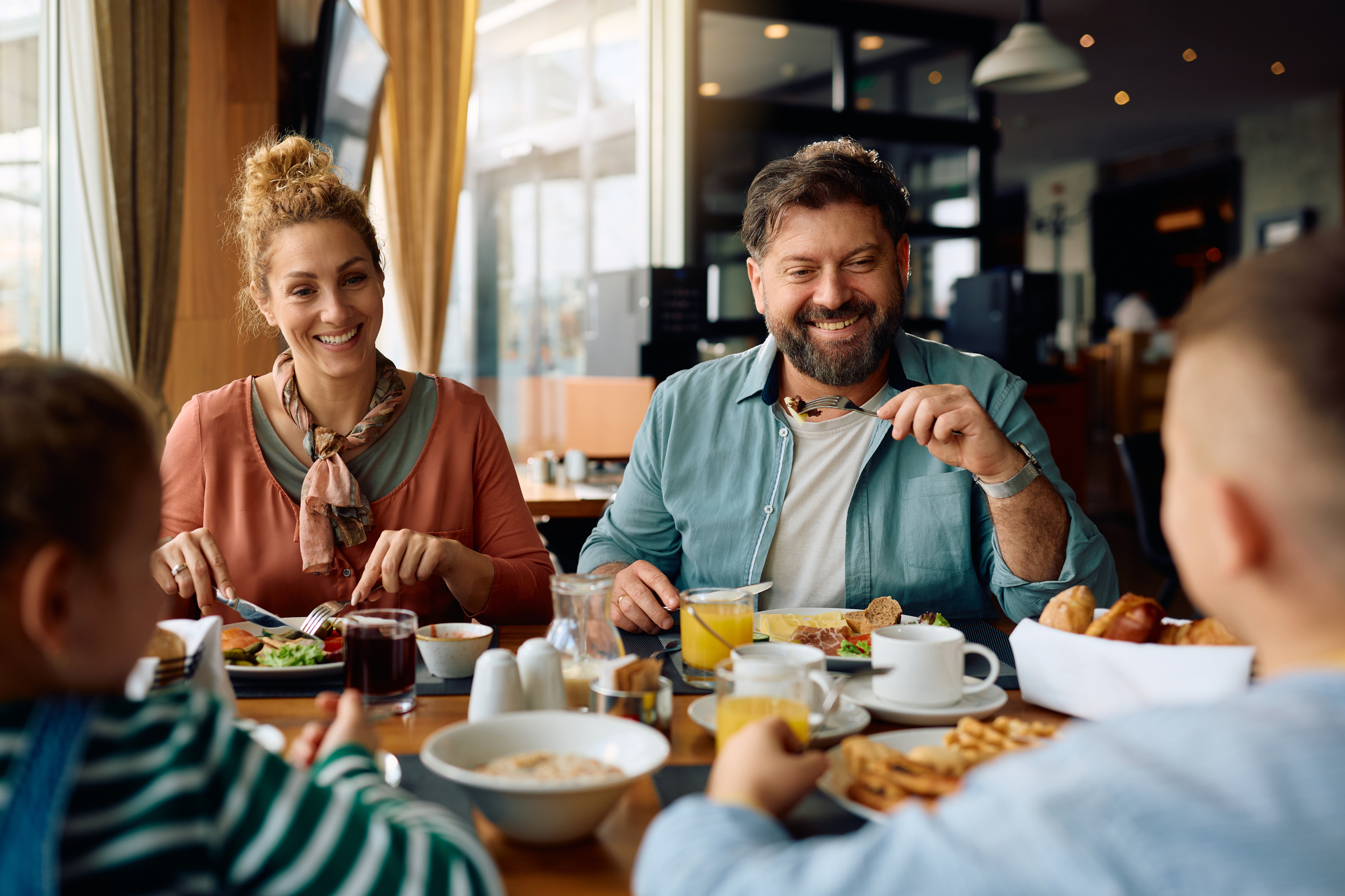 Family sitting at a table in a hotel, eating breakfast with coffee, bread and waffles
