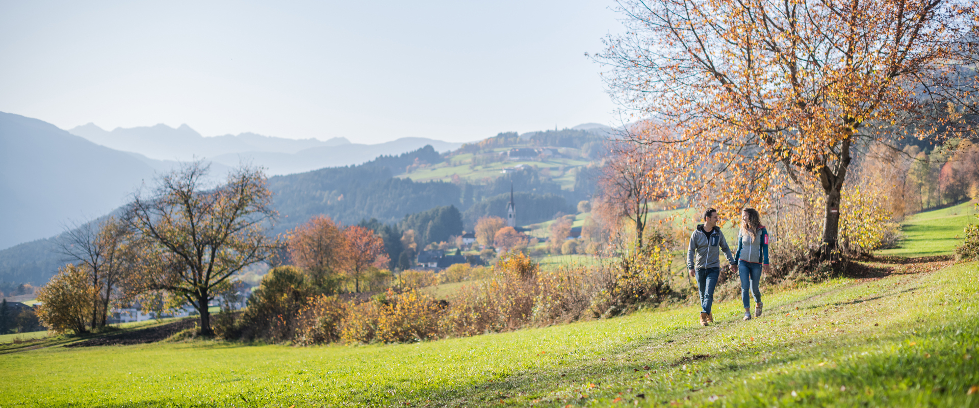 A woman and a man are walking walks through the colourful autumn landscape overlooking Pfalzen near Bruneck.